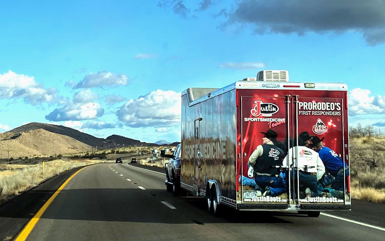 A red, black and white trailer driving away from the camera into the blue skies on the road.